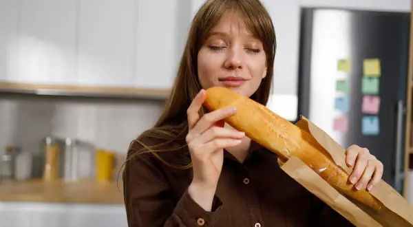 Kobieta wącha świeżą bagietkę, zastanawiając się, jakie choroby powoduje gluten.