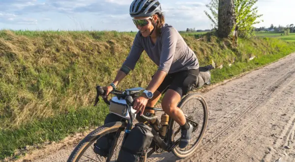 Kobieta w kasku i okularach przeciwsłonecznych jedzie na rowerze po piaszczystej drodze. To przygoda z rowerem w okolicach Gdańska.
