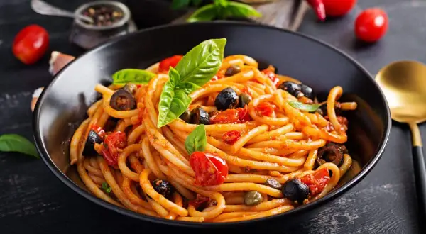 Un plat de pâtes aux anchois, tomates, olives et câpres, garni de basilic frais. Un délice méditerranéen.