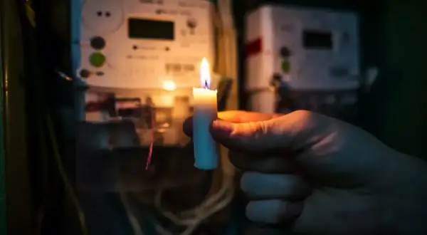 Gdy najemca nie płaci czynszu, można odłączyć mu media. Płonąca świeca w dłoni na tle liczników energii elektrycznej symbolizuje brak prądu.