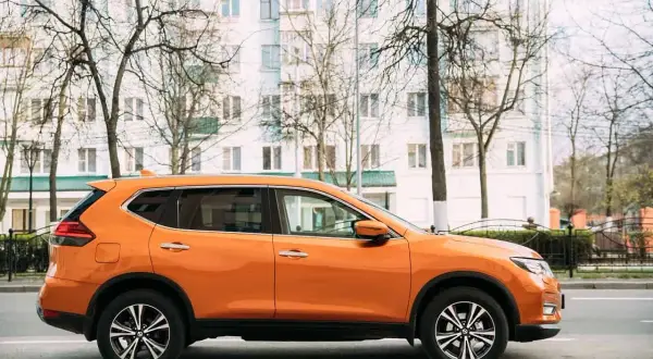 Pomarańczowy SUV do 50 tys. zaparkowany na tle białego budynku i drzew.