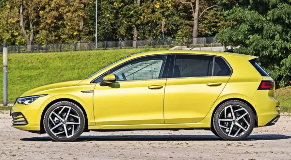 Żółty hatchback stoi na tle zieleni i drzew.