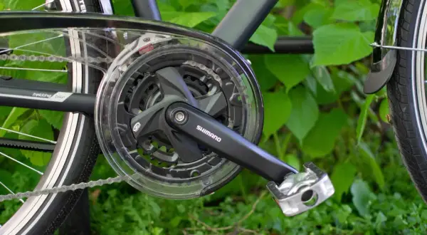 Część napędu roweru trekkingowego Shimano z korbą i zębatkami. Gotowy do jazdy po zielonym tle.