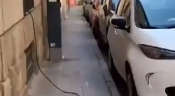 Un coche eléctrico en carga, con cables cruzando la acera, obstaculizando el paso.