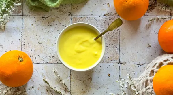 Crema gialla e liscia in una ciotola, con arance fresche intorno. Un cucchiaio dorato è immerso nella crema, che ricorda il sapore del sale all'arancia.
