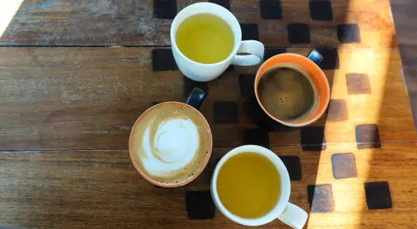 Kawa i herbata na drewnianym stole. Czy zielona herbata pobudza? Obok kawy latte i espresso, dwie filiżanki zielonej herbaty.