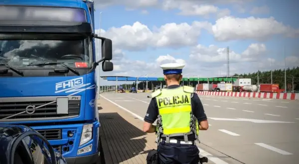 Policjant w kamizelce odblaskowej przy niebieskiej ciężarówce Volvo FH13. W tle przejście graniczne, kategoria c.
