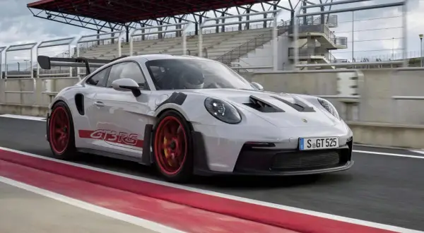 Biały Porsche 992 GT3 RS z czerwonymi akcentami i felgami pędzi po torze wyścigowym.