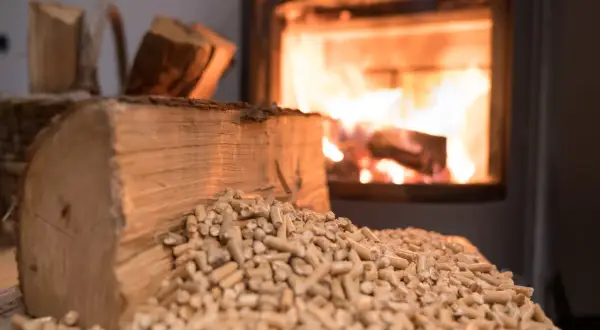 Holzscheite und Pellets liegen vor einem brennenden Ofen. Ob Birke, Hartholz oder Weichholz, die Wärme ist spürbar.