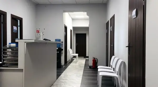 Korytarz centrum medycznego z recepcją, drzwiami i białymi krzesłami.