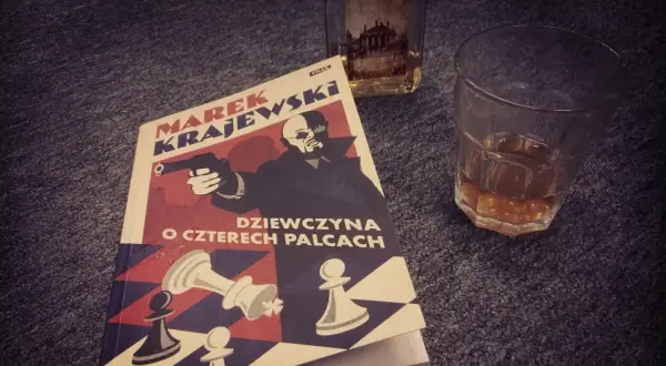 Powieść Marka Krajewskiego "Dziewczyna o czterech palcach" leży obok szklanki z bursztynowym trunkiem.