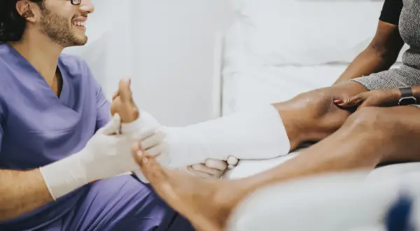 Medico sorridente applica una fasciatura a un paziente con un malleolo gonfio.