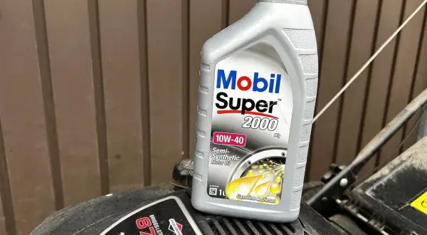 Butelka oleju Mobil Super 2000 10W-40 na silniku kosiarki Briggs & Stratton.