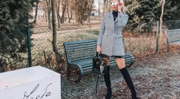 Elegancka sukienka w pepitkę, idealna na jesienne stylizacje. Kobieta w okularach przeciwsłonecznych i kozakach prezentuje modny zestaw.