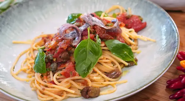 Spaghetti Puttanesca mit Sardellen, Oliven, Kapern und frischem Basilikum auf einem Teller.