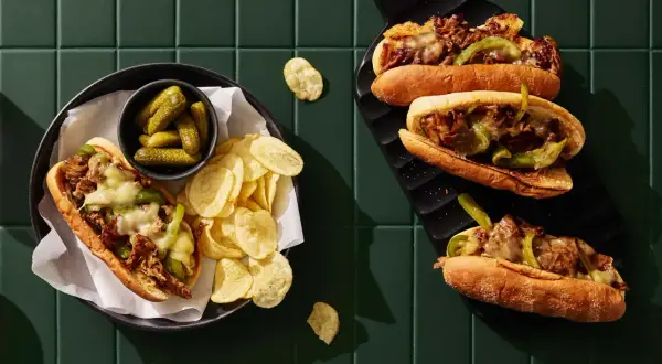 Två philly cheese steak-mackor med smält ost, paprika och lök. Serveras med cornichoner och potatischips.