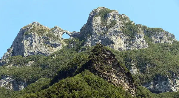 Il monte forato, con la sua roccia scolpita dal vento, si erge maestoso tra il verde della vegetazione e l'azzurro del cielo.