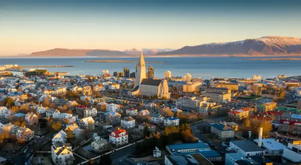 Fakta om Island: Reykjaviks ikoniska kyrka Hallgrímskirkja reser sig över staden med havet och snöklädda berg i bakgrunden.