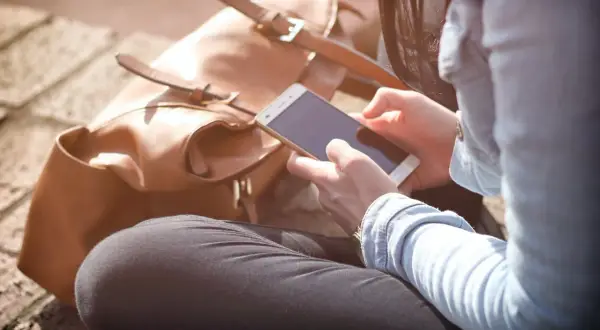 Kobieta z telefonem w dłoniach, obok brązowa torba. Ikona słuchawka z wifi jak wyłączyć.