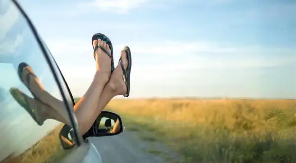 Pieds en claquettes sortant de la fenêtre d'une voiture, profitant du voyage par une journée ensoleillée.