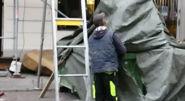 Pracownik w kamizelce i czapce przykrywa coś zieloną plandeką. Czy to hałas?
