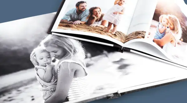 Otwarta fotoksiążka i fotoalbum prezentują rodzinne chwile: mama z dzieckiem na czarno-białym zdjęciu i rodzice z córką na plaży.