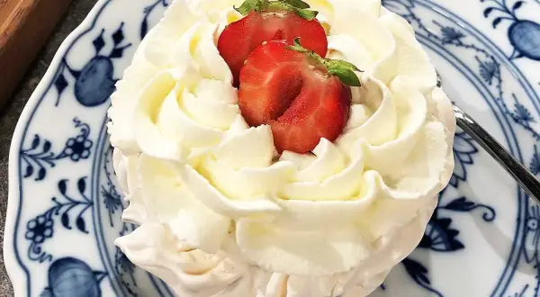 En liten pavlova med fluffig grädde och färska jordgubbar på en vacker blåvit tallrik. En perfekt liten dessert!