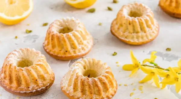 Szybkie babeczki wielkanocne, oprószone cukrem pudrem, z cytryną i pistacjami w tle.