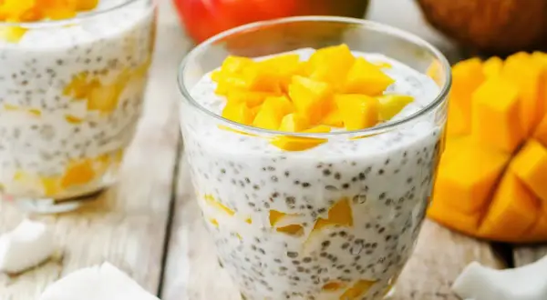 Pyszny deser chia z mlekiem kokosowym i kawałkami mango, podany w szklance. Obok świeże mango i wiórki kokosowe.