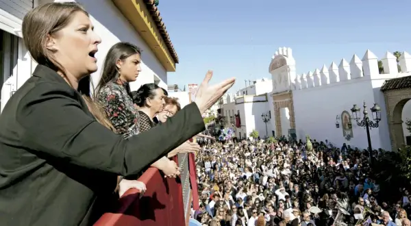 Mujeres en un balcón observan una multitud y escuchan saetas populares.