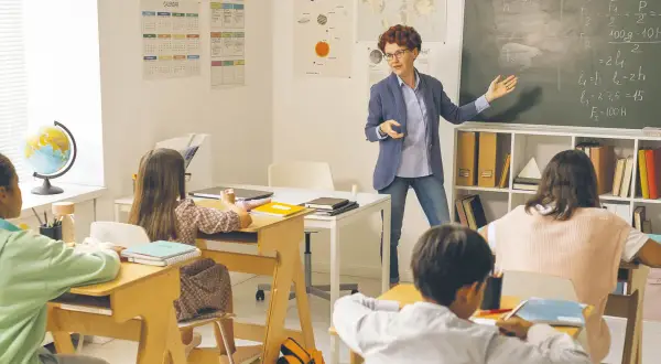 Nauczycielka tłumaczy zadanie, dzieci słuchają. Ile godzin tygodniowo pracuje nauczyciel przedszkola? To pytanie pozostaje bez odpowiedzi, ale lekcja trwa.