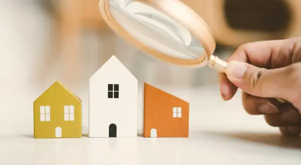 Lente d'ingrandimento esamina tre casette di legno, evidenziando la differenza tra cessione e subentro nel mercato immobiliare.