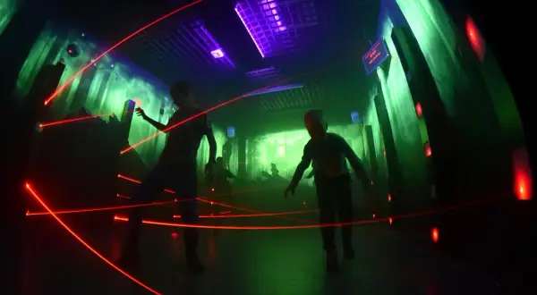 Dzieci bawią się w laserowym labiryncie w Krakowie, unikając czerwonych promieni.