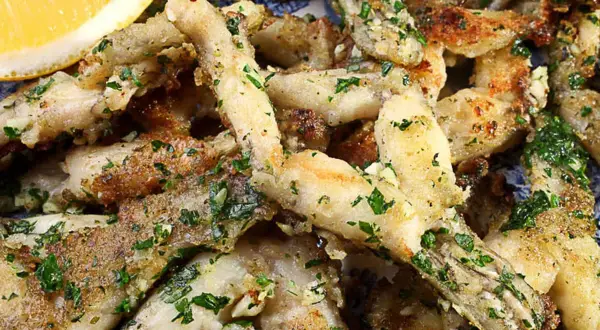 Un plat de cuisse de grenouille frite, garni de persil frais et d'ail, servi avec un quartier de citron.
