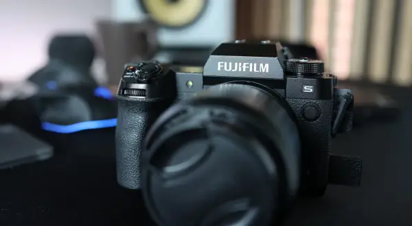 Czarny aparat Fujifilm xh2s z obiektywem i osłoną obiektywu na czarnym blacie.