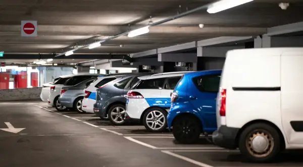 Montaż czujników parkowania w garażu podziemnym. Rzędy samochodów, w tym biała furgonetka, niebieski hatchback i kilka innych pojazdów, stoją na miejscach parkingowych.