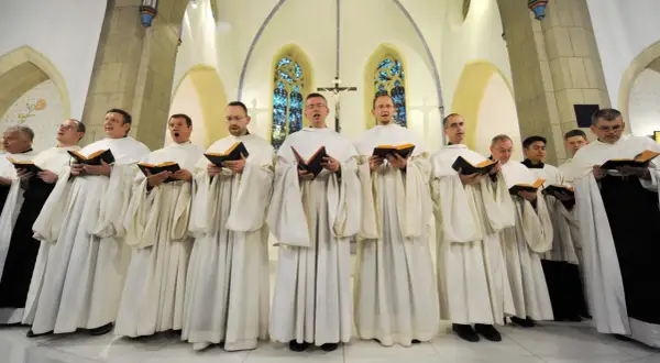 Mönche in weißen Roben singen gregorianik musik aus Büchern in einer Kirche.