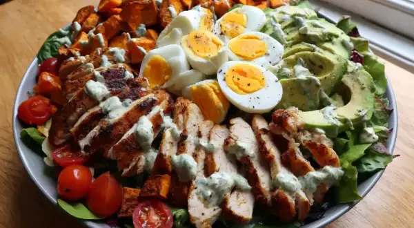 En stor, matig sallad med grillad kyckling, ägg, sötpotatis, avokado och körsbärstomater, toppad med en krämig dressing.
