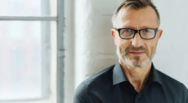 Man med glasögon och skägg, klädd i svart skjorta. Perfekt för bra profilbilder som ger ett professionellt intryck.