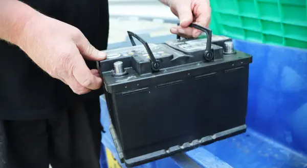Händer placerar ett bilbatteri i en blå behållare. Kanske för återvinning eller för att byta ut dubbla batterier i bilen.