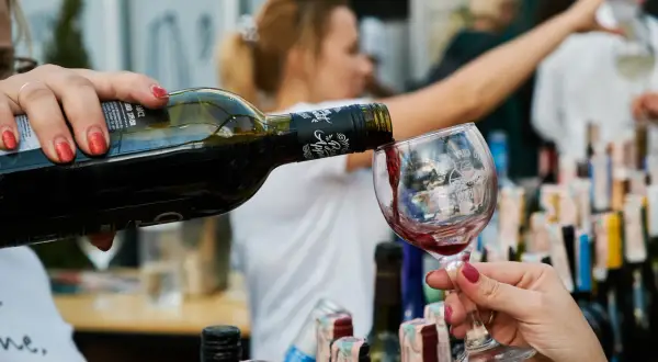 Rödvin hälls upp i ett glas, perfekt vin till lutfisk. Bakgrunden visar en festlig sammankomst med fler vinflaskor.
