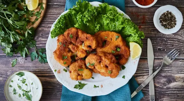 Knuspriges Blumenkohl Schnitzel mit frischem Salat, Zitrone und Dip. Ein Genuss für Vegetarier!