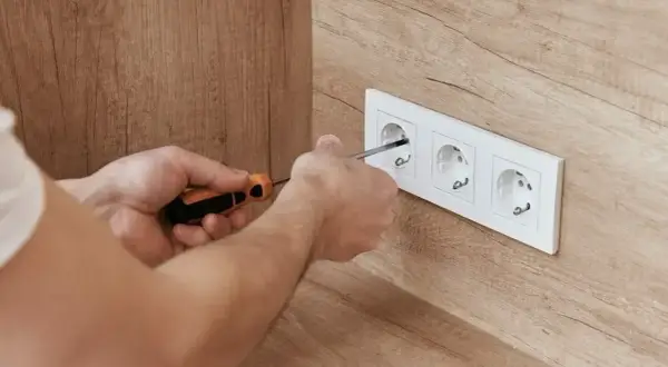 Ręce przykręcają gniazdko elektryczne. Wkrętak precyzyjnie pracuje, zapewniając bezpieczne napięcie skuteczne.