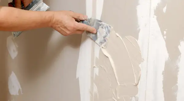 Mano stende stucco su una giuntura di cartongesso, ricordando che il cartongesso ha un verso.