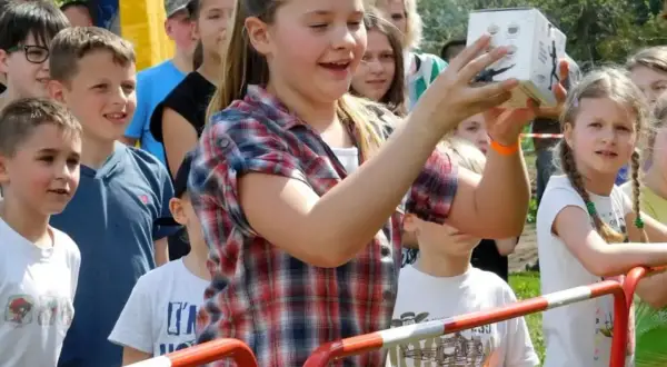 Dziewczynka trzyma pudełko na festynie rodzinnym, otoczona innymi dziećmi.