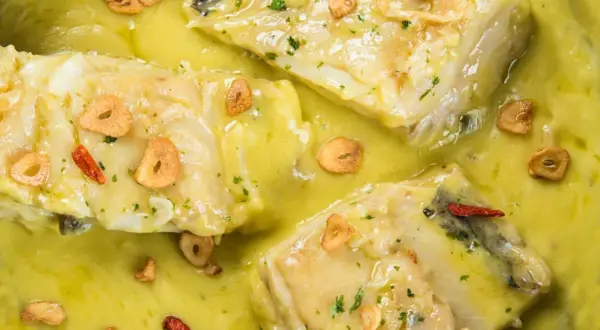 Merluza al pil pil, con trozos de pescado blanco en una salsa amarilla cremosa, adornada con láminas de ajo crujiente y guindilla.