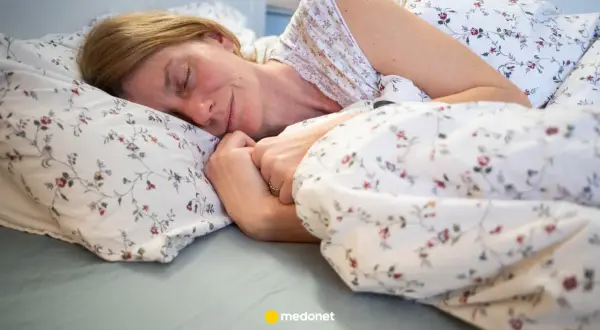 Kobieta zasypia w łóżku, otulona pościelą w kwiaty. To idealny moment na czytanie przed snem.