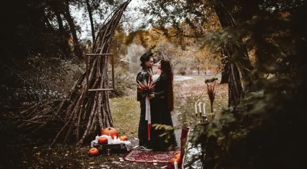 Para w czarnych strojach pod łukiem z gałęzi, dynie i świece.