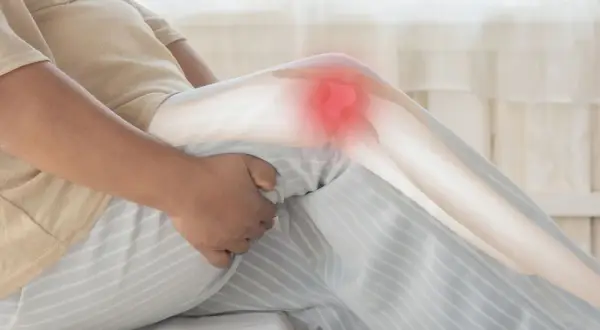 Une personne tient son genou, marqué d'une zone rouge, suggérant une douleur au genou au repos la nuit.
