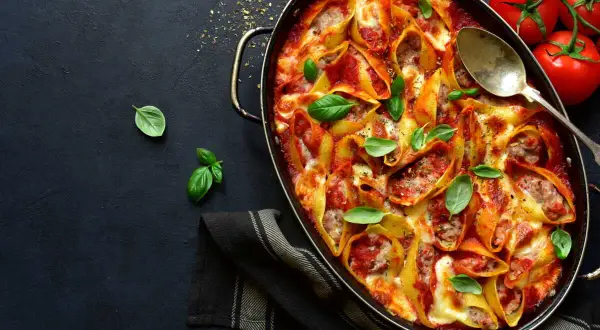 Conchiglioni farcis à la sauce tomate et au fromage, prêts à faire lever la pâte au four. Garnis de basilic frais.